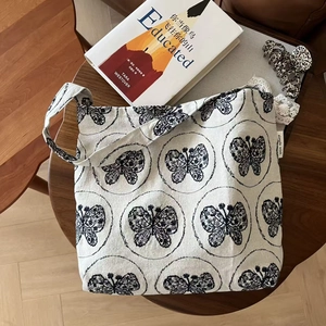 Cream canvas tote bag with black butterfly embroidery, lace edges, and simple wish label
