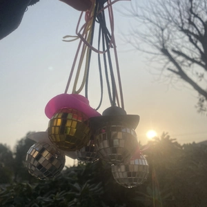 Nahaufnahme funkelnder Discokugel-Anhänger mit bunten Mini-Hüten im goldenen Sonnenlicht