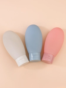 Three silicone travel bottles in grey blue and pink shown on an orange background