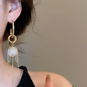 Detail of elegant gold tassel earrings with large white pearl and delicate metal chains