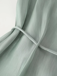 Close-up of sage green semi-transparent fabric texture with bow-tie detail on the shirt