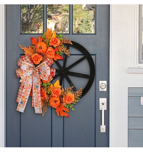Close-up of autumn wreath with orange pumpkins and maple leaves on a black wagon wheel base