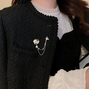 Détail d'une broche à pampilles fleur et papillon dorée sur une veste en tweed