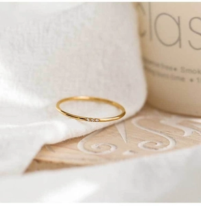 Detail of a slim gold-plated ring featuring three micro-set zircons on a wooden texture