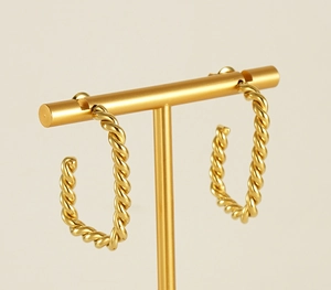 Detailed view of 18K gold-plated twisted rope C-shaped earrings on a golden display stand