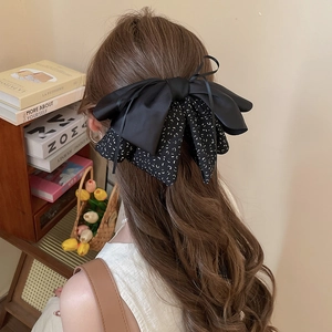 Detail of a large layered black satin and polka dot bow hair clip on a model's hair