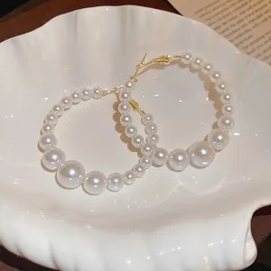 Elegant gold hoop earrings with gradient white pearls displayed on a white shell tray