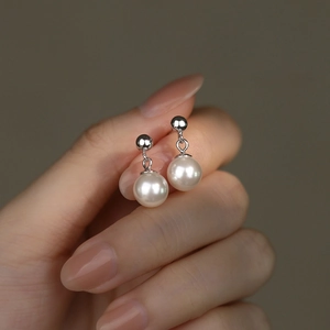 Elegant S925 sterling silver pearl drop earrings held by hand on a dark background