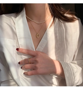 Macro shot of layered gold oval pendant necklace and pearl choker on white shirt
