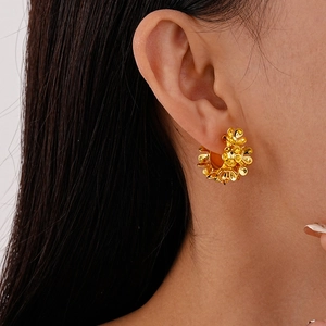 Close-up of golden floral stud earrings with a shiny metallic finish worn by a model