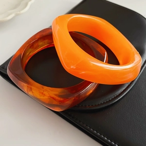 Close-up of square resin bracelets in bright orange and translucent amber finishes
