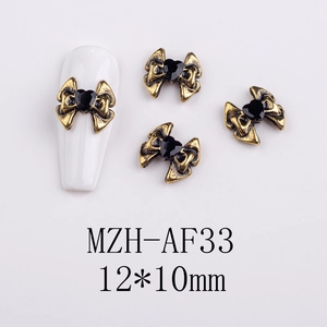 Detail of vintage gold bow nail art charm with black heart gemstone on white nail tip