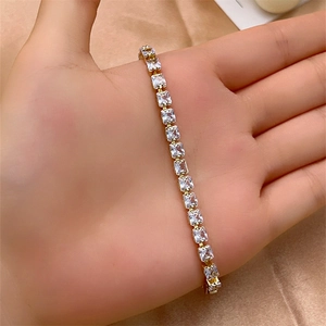 Detail of gold tennis bracelet with square-cut clear crystals on champagne silk background
