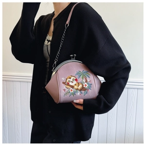 Detail of embroidered shell bag with sloth pattern and metal chain strap on model