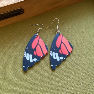 Detail view of acrylic butterfly wing earrings with red and black patterns on green fabric