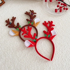 Close-up of red and brown reindeer antler headbands with holly leaves on white plush background