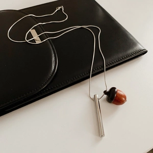 Detail shot of a silver metal cylinder and dark wooden acorn pendant on black leather