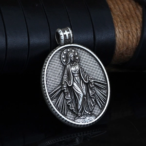 Macro shot of silver Virgin Mary oval pendant with cross bail on reflective black surface
