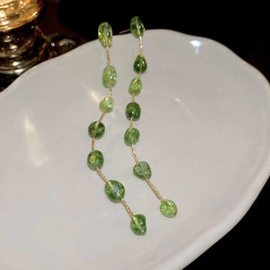 Long earrings with green irregular stones and gold chains in a ceramic dish