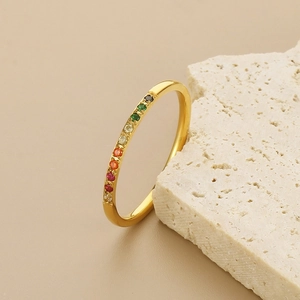 Detailed macro view of thin golden rainbow ring with colorful gemstones on a white stone
