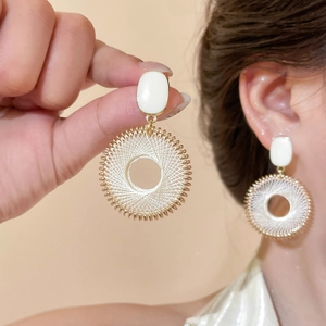 Détail de boucles d'oreilles quadrillées blanc et or présentées à la main et sur modèle