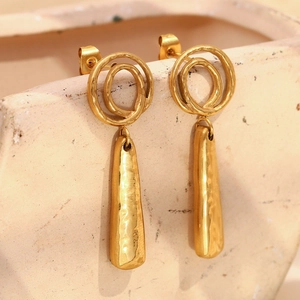 Vue macro de boucles d'oreilles dorées texturées suspendues sur un vase en céramique