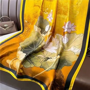 Elegant yellow silk scarf with lotus print displayed on a brown leather sofa