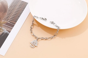 Silver Hamsa Hand bracelet with hollow patterns on a white plate and orange background