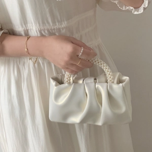 Close-up of pearl handle detail on white pleated cloud bag with elegant satin finish