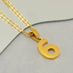 Macro view of a gold-tone number 6 pendant necklace on a reflective surface