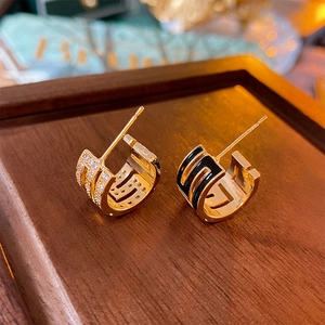 Detailed close-up of gold-plated asymmetric C-shape earrings with black enamel and zircons