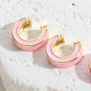 Macro shot of gold-plated C-shaped earrings with light pink enamel on stone base