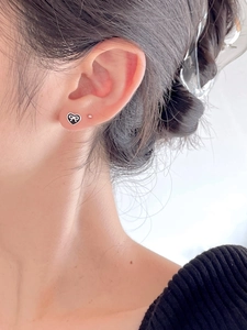 Detail showing a black heart stud with white bow and silver bead on a model ear