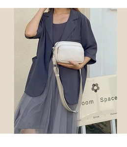 Side view of beige crossbody bag with dual-zipper layers and adjustable wide strap