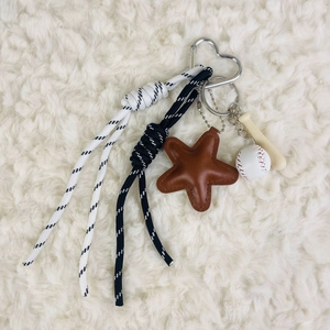 Detail of keychain featuring brown leather star, baseball charms and woven strap