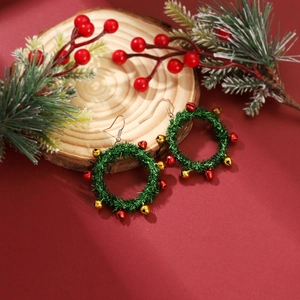 Close-up of festive Christmas wreath earrings with red and gold bells on wood