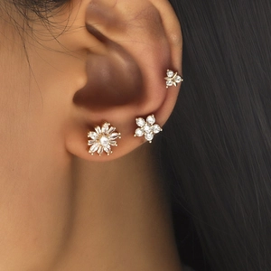 Close-up of golden flower stud earrings set with zircon stones on a female ear