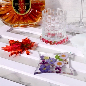 Detailed view of leaf and geometric resin coasters with embedded dried flowers on wood