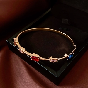 Detail of 18K gold-plated bangle with colorful inlaid gemstones on dark silk backdrop