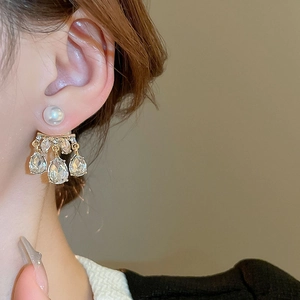 Macro side view of elegant pearl and drop-shaped crystal earrings on female model