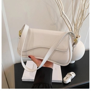 Close-up of white leather shoulder bag with gold hardware buckle and adjustable strap