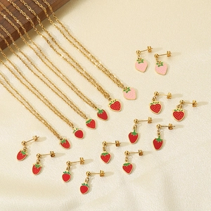 Gold strawberry pendant necklace and earring jewelry set on beige textured fabric