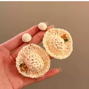 Close-up of hand holding a woven straw hat earring with detailed floral accents