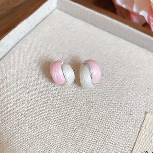 Macro shot of pink and pearly white C-shaped stud earrings on a linen jewelry display