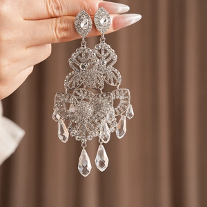 Detailed close-up of silver floral earrings with crystal teardrop tassels being held
