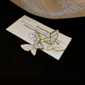 Macro shot of gold butterfly earrings with white enamel and zircon on vintage card