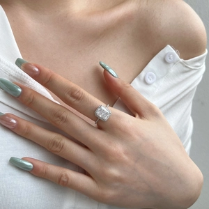 Close-up of cushion-cut halo engagement ring with pavé diamonds on a model's finger