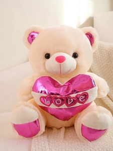 Macro detail of plush teddy bear holding a metallic pink heart with LOVE embroidery