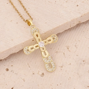 Detailed close-up of 18K gold-plated cross pendant with micro-set cubic zirconia on travertine
