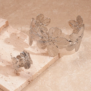 Detail of silver metallic flower cuff bracelet and ring set on marble display